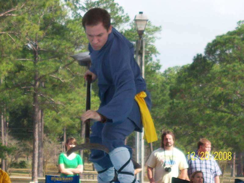 Joshua outdoors in a blue outfit and yellow sash holding a pole